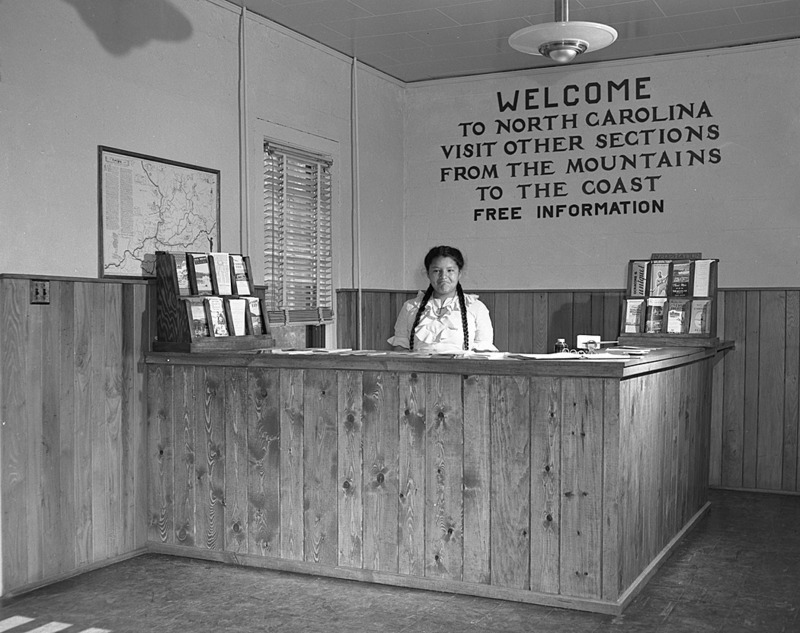 Girl at Information Booth, Cherokee Information Center, Cherokee Reservation, Swain Co., June 1947. This photo is part of a collection of photos promoting traveling and tourism in North Carolina, taken by photographers who worked for the Department of Conservation and Development, Division of Travel Information.